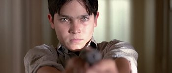 Movie still from “Road to Perdition” (2002), directed by Sam Mendes – A young man is holding a gun and looking at the camera; Close Up shot, Low angle