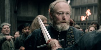 Movie still from “The Witcher” (2019), created by Lauren Schmidt Hissrich – A bearded man holding a sword in a crowd of people; Close Up shot, Over the shoulder angle