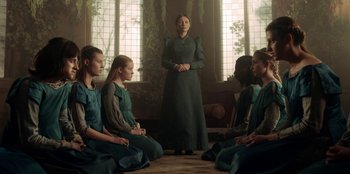Movie still from “The Witcher” (2019), created by Lauren Schmidt Hissrich – A group of people sitting in a circle with a woman in front of them; Medium shot, Low angle