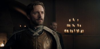 Movie still from “The Witcher” (2019), created by Lauren Schmidt Hissrich – A man in a leather jacket standing next to a man in a robe; Close Up shot, Over the shoulder angle