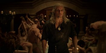 Movie still from “The Witcher” (2019), created by Lauren Schmidt Hissrich – A man with long blonde hair standing in front of a group of people; Medium shot, High angle