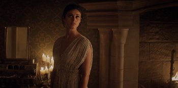 Movie still from “The Witcher” (2019), created by Lauren Schmidt Hissrich – A woman standing in front of a pillar and candles; Medium shot, Over the shoulder angle