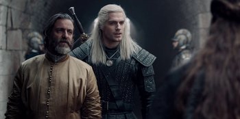 Movie still from “The Witcher” (2019), created by Lauren Schmidt Hissrich – A man in a leather jacket holding a sword in his hand; Medium shot, Over the shoulder angle