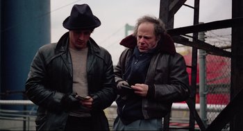 Movie still from “Rocky” (1976), directed by John G. Avildsen – Two men standing next to each other looking at their cell phones; Medium shot, Low angle