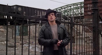 Movie still from “Rocky” (1976), directed by John G. Avildsen – A man wearing a black hat standing in front of a fence; Medium shot, Low angle