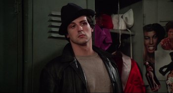 Movie still from “Rocky” (1976), directed by John G. Avildsen – A man wearing a black hat and a leather jacket; Close Up shot, Over the shoulder angle
