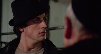 Movie still from “Rocky” (1976), directed by John G. Avildsen – A man in a hat is looking into a mirror; Close Up shot, Over the shoulder angle