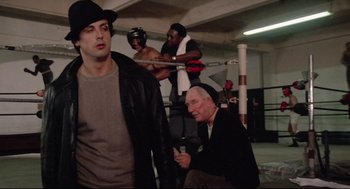 Movie still from “Rocky” (1976), directed by John G. Avildsen – A group of people in a boxing ring; Medium shot, Over the shoulder angle