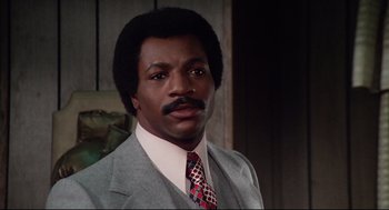 Movie still from “Rocky” (1976), directed by John G. Avildsen – A man in a gray suit and a red tie; Close Up shot, Low angle