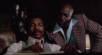 Movie still from “Rocky” (1976), directed by John G. Avildsen – A couple of men sitting next to each other in a room; Medium shot, Low angle