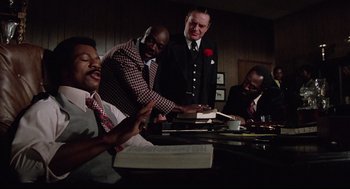 Movie still from “Rocky” (1976), directed by John G. Avildsen – A group of men sitting at a table reading books; Medium shot, Low angle
