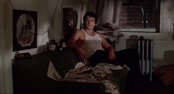 Movie still from “Rocky” (1976), directed by John G. Avildsen – A man sitting on top of a couch next to a pile of newspapers; Wide shot, Low angle