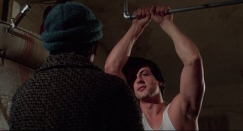 Movie still from “Rocky” (1976), directed by John G. Avildsen – A man is holding onto a bar while another man looks on; Medium shot, Over the shoulder angle