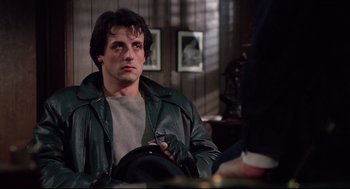 Movie still from “Rocky” (1976), directed by John G. Avildsen – A man in a leather jacket holding a hat; Medium shot, Over the shoulder angle