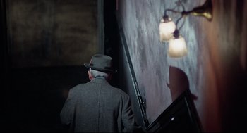 Movie still from “Rocky” (1976), directed by John G. Avildsen – An older man in a hat and a suit walking in front of a projection screen; Medium shot, Low angle