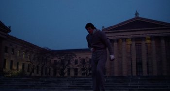 Movie still from “Rocky” (1976), directed by John G. Avildsen – A man walking down steps in front of a building; Wide shot, Low angle