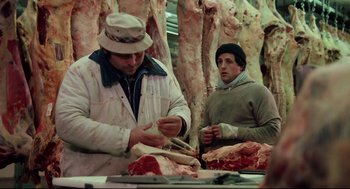 Movie still from “Rocky” (1976), directed by John G. Avildsen – Two men are working in a meat market; Medium shot, High angle