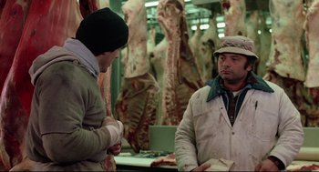 Movie still from “Rocky” (1976), directed by John G. Avildsen – Two men are talking in a meat market; Medium shot, Low angle