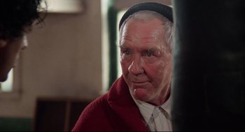 Movie still from “Rocky” (1976), directed by John G. Avildsen – An older man wearing a red sweater and a black hat; Close Up shot, Low angle