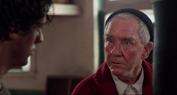 Movie still from “Rocky” (1976), directed by John G. Avildsen – An old man wearing a red sweater and a black hat; Close Up shot, Over the shoulder angle