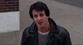 Movie still from “Rocky” (1976), directed by John G. Avildsen – A man in a leather jacket standing on the sidewalk; Close Up shot, Low angle