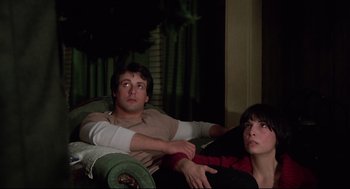 Movie still from “Rocky” (1976), directed by John G. Avildsen – A man and a woman sitting on a couch watching tv; Medium shot, Low angle