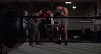 Movie still from “Rocky” (1976), directed by John G. Avildsen – Three men are boxing in a boxing ring; Wide shot, Low angle