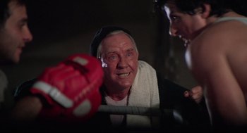 Movie still from “Rocky” (1976), directed by John G. Avildsen – An older man wearing a white shirt and a black hat; Close Up shot, Over the shoulder angle