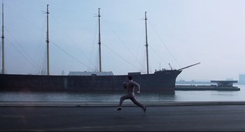 Movie still from “Rocky” (1976), directed by John G. Avildsen – A man is running on the side of the road near a boat; Extreme Wide shot, High angle