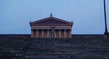 Movie still from “Rocky” (1976), directed by John G. Avildsen – A man standing on top of steps in front of a building; Extreme Wide shot, Low angle