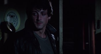Movie still from “Rocky” (1976), directed by John G. Avildsen – A man in a leather jacket standing next to a wall; Close Up shot, Over the shoulder angle
