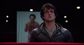 Movie still from “Rocky” (1976), directed by John G. Avildsen – A man in a black leather jacket stands in a boxing ring; Medium shot, Low angle