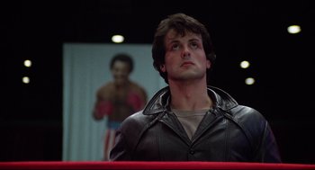 Movie still from “Rocky” (1976), directed by John G. Avildsen – A man in a black leather jacket looking up; Medium shot, Low angle
