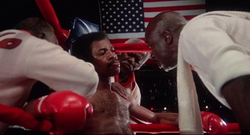 Movie still from “Rocky” (1976), directed by John G. Avildsen – A group of men in a boxing ring with an american flag in the background; Medium shot, Low angle