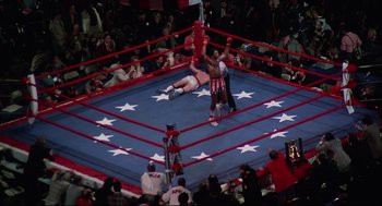 Movie still from “Rocky” (1976), directed by John G. Avildsen – Two men are wrestling in a boxing ring while people watch; Wide shot, Overhead angle