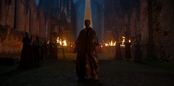 Movie still from “The Witcher” (2019), created by Lauren Schmidt Hissrich – A man dressed as a wizard standing in front of fire; Extreme Wide shot, Low angle
