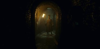 Movie still from “The Witcher” (2019), created by Lauren Schmidt Hissrich – A man holding a torch in a dark tunnel; Wide shot, Low angle