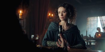 Movie still from “The Witcher” (2019), created by Lauren Schmidt Hissrich – A woman sitting at a table with a wine glass in front of her; Close Up shot, Over the shoulder angle