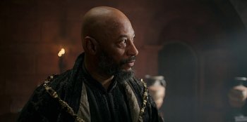 Movie still from “The Witcher” (2019), created by Lauren Schmidt Hissrich – A bald man with a beard and a black robe; Close Up shot, Over the shoulder angle