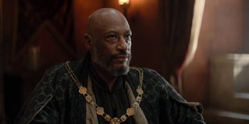 Movie still from “The Witcher” (2019), created by Lauren Schmidt Hissrich – An older man with a beard wearing a gold necklace; Close Up shot, Over the shoulder angle