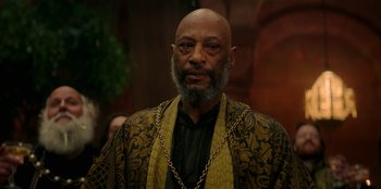 Movie still from “The Witcher” (2019), created by Lauren Schmidt Hissrich – An older man with a beard and a long chain around his neck; Close Up shot, Over the shoulder angle