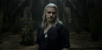 Movie still from “The Witcher” (2019), created by Lauren Schmidt Hissrich – A man with long white hair standing in the woods; Medium shot, High angle