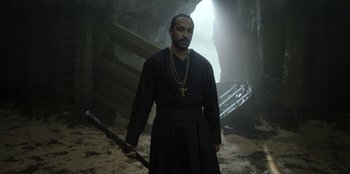 Movie still from “The Witcher” (2019), created by Lauren Schmidt Hissrich – A man holding a sword wearing a black robe; Medium shot, Low angle