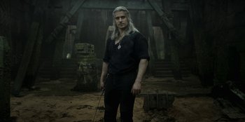 Movie still from “The Witcher” (2019), created by Lauren Schmidt Hissrich – A man in a black shirt holding a sword; Medium shot, Low angle
