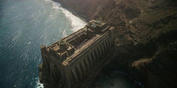 Movie still from “The Witcher” (2019), created by Lauren Schmidt Hissrich – An aerial view of an abandoned building near the ocean; Extreme Wide shot, High angle