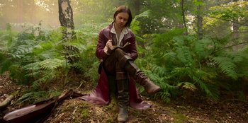 Movie still from “The Witcher” (2019), created by Lauren Schmidt Hissrich – A man sitting on the ground in the woods writing; Medium shot, Low angle