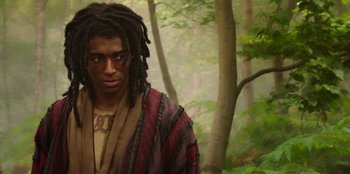 Movie still from “The Witcher” (2019), created by Lauren Schmidt Hissrich – A man with dreads standing next to a forest; Medium shot, Low angle