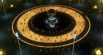 Movie still from “The Wiz” (1978), directed by Sidney Lumet – An aerial view of a group of people standing in a circle in front of a globe; Extreme Wide shot, High angle