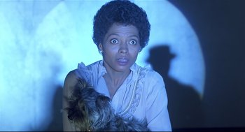 Movie still from “The Wiz” (1978), directed by Sidney Lumet – A woman holding a dog in front of a projector screen; Close Up shot, Low angle