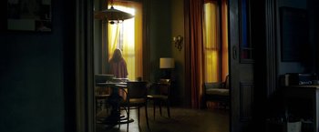 Movie still from “The Woman in the Window” (2021), directed by Joe Wright – A woman sitting at a table looking out of a window; Wide shot, High angle